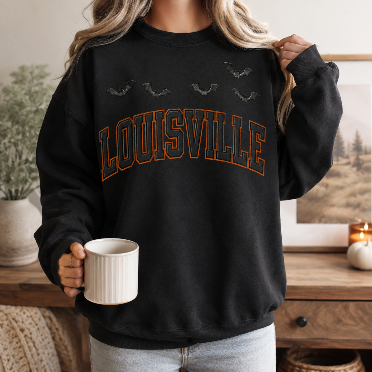Louisville Halloween blackout crewneck in Black — worn on model holding a mug in a fall interior