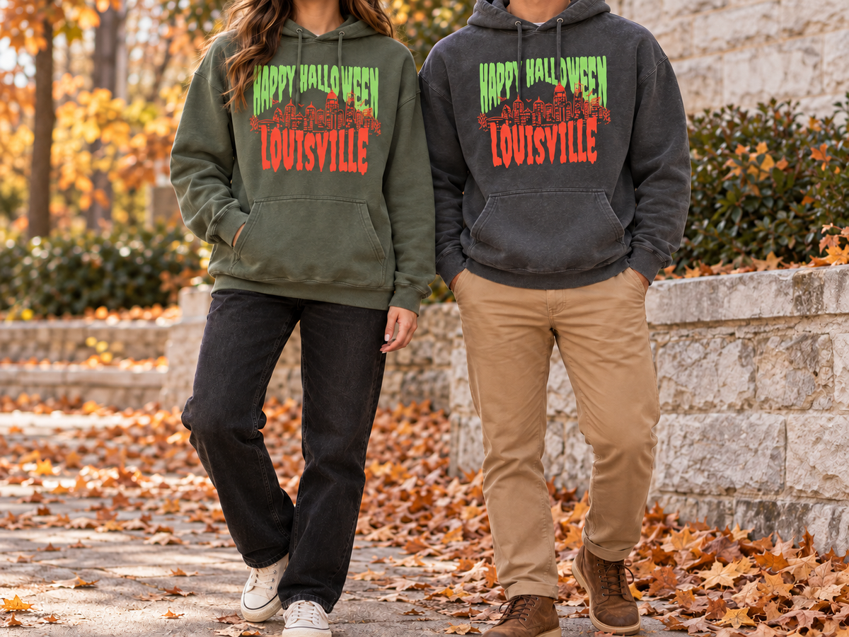 Couple in autumn leaves wearing the Louisville Halloween Spooky Skyline hoodie in Moss and in Pepper