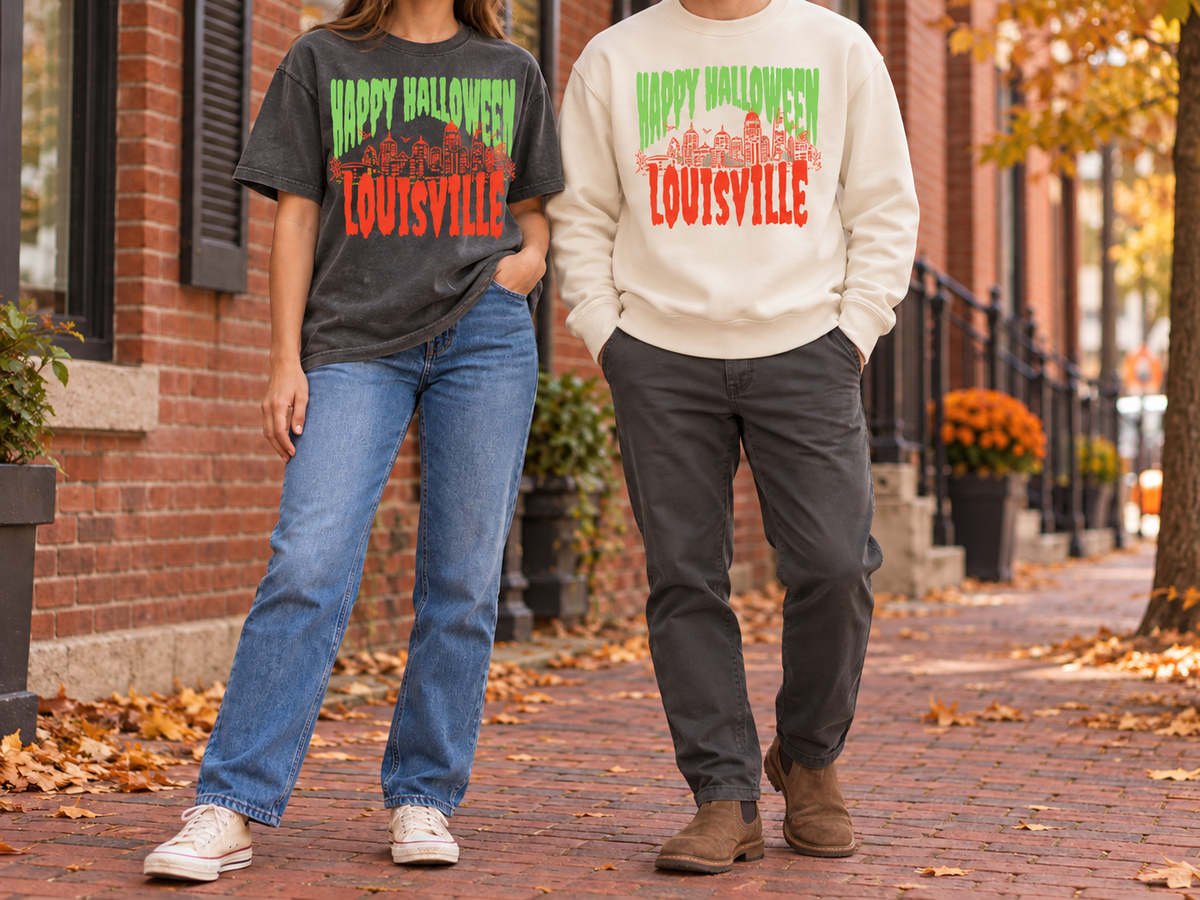 Couple on a brick sidewalk in fall wearing the Louisville Halloween Spooky Skyline Comfort Colors tee in Pepper and the crewneck sweatshirt in Ivory